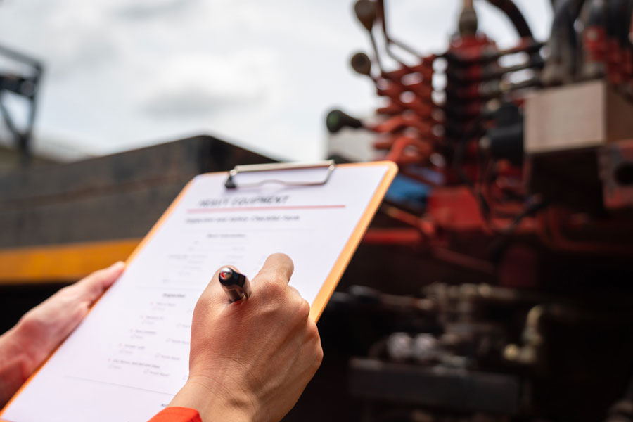 A person holds a clipboard and pen, checking off items on a checklist in front of industrial machinery